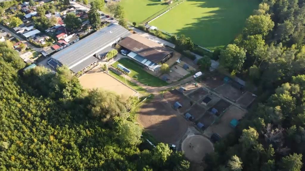 Luftbild der Reitanlage des Reitclub Fischbach mit Reithalle, Stallzeile, Dressurviereck, Paddocks und Roundpen, eingebettet in den Wald